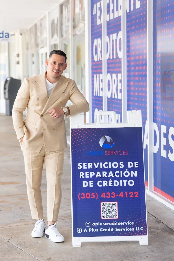 Un miembro del equipo junto al letrero de A Plus Credit Services, afuera de la oficina de Coral Way